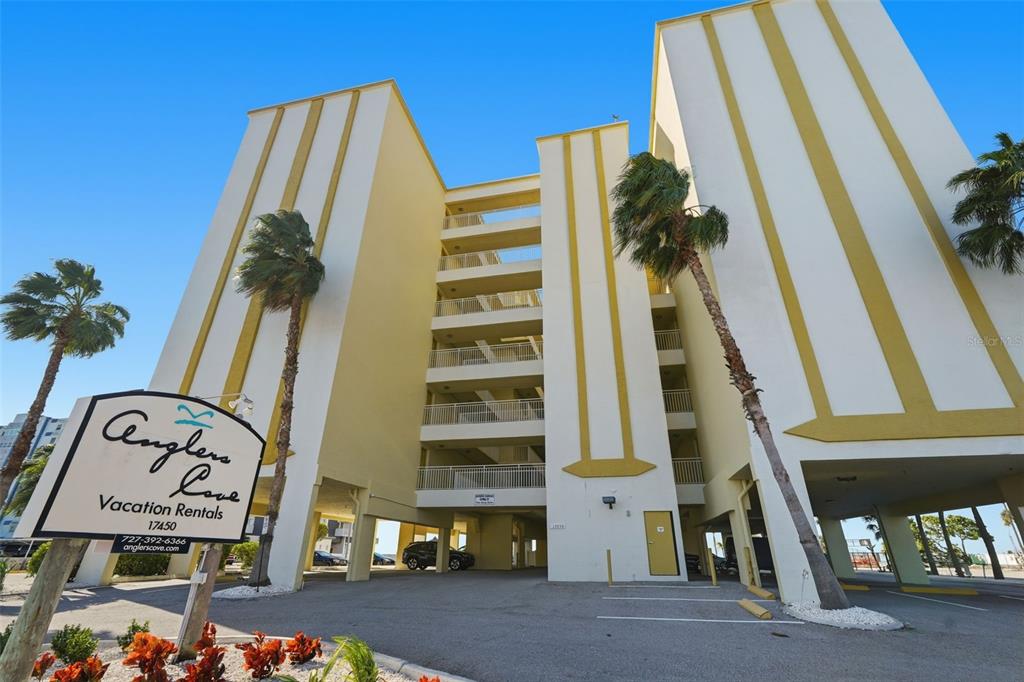 A low-angle exterior view of a multi-story apartment building with a sign for vacation rentals — 17450 GULF BOULEVARD UNIT 104, REDINGTON SHORES, FL