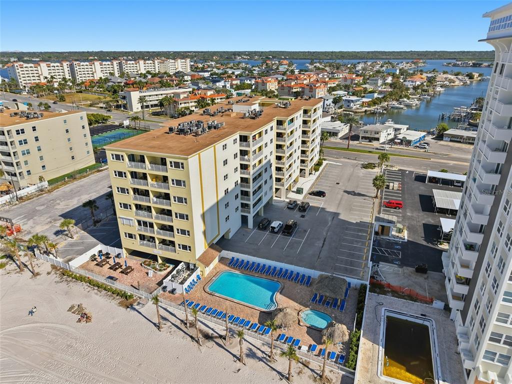 An aerial view shows a multi-story apartment building with a pool, parking lot, and beach — 17450 GULF BOULEVARD UNIT 104, REDINGTON SHORES, FL