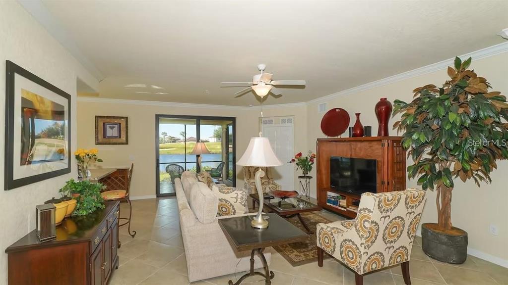 A living room features tile floors, a ceiling fan, patterned armchairs, and a sliding glass door — 6614 GRAND ESTUARY TRAIL UNIT 101, BRADENTON, FL