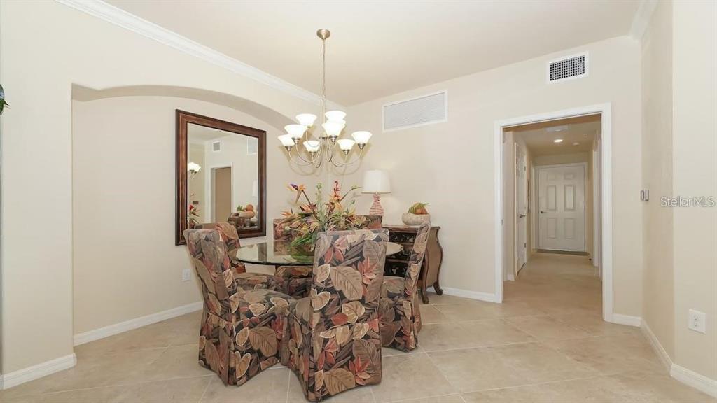 A dining room features a glass-topped table, patterned chairs, a chandelier, and tile flooring — 6614 GRAND ESTUARY TRAIL UNIT 101, BRADENTON, FL