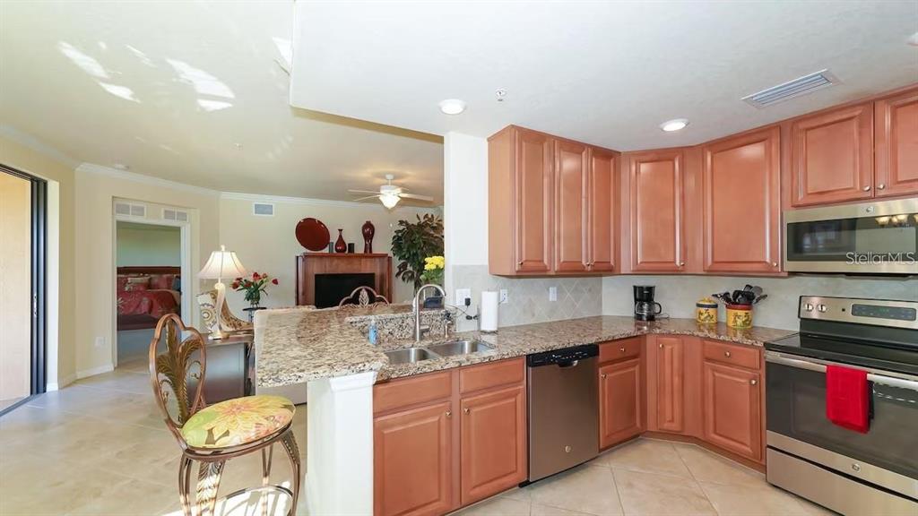 A kitchen with wood cabinets, granite countertops, and stainless steel appliances opens to a living area — 6614 GRAND ESTUARY TRAIL UNIT 101, BRADENTON, FL