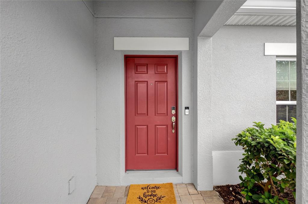 A red front door with a welcome mat sits on a paved porch — 1181 STRATTON AVENUE, GROVELAND, FL