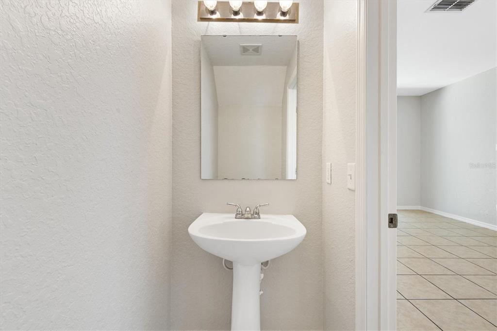 A small bathroom features a white pedestal sink, a wall-mounted mirror, and vanity lighting — 5186 NE 122ND BOULEVARD, OXFORD, FL