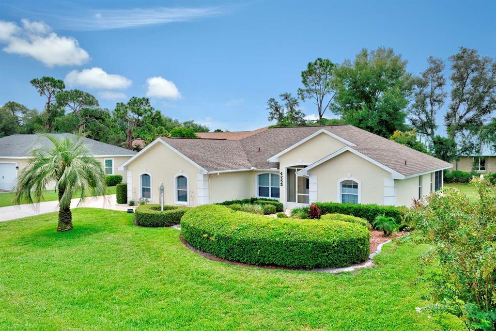 A single-story house with a beige exterior, a shingled roof, and a manicured hedge garden — 4253 CREMONA DRIVE, SEBRING, FL