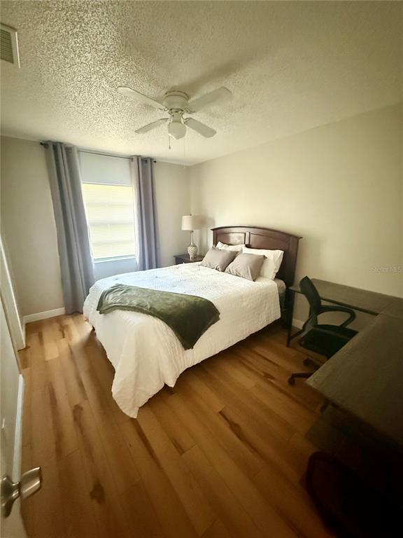 A bedroom features a bed, a desk with a chair, and wood-look flooring — 9402 N SEMMES STREET, TAMPA, FL