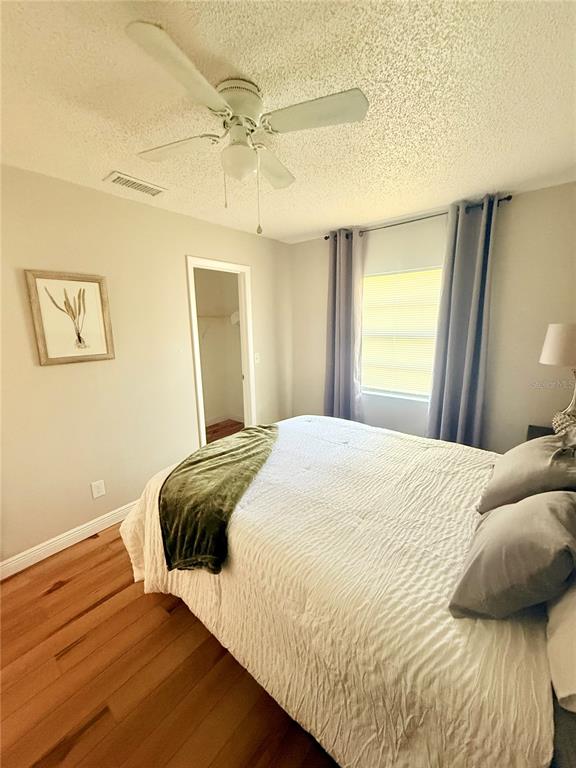 A bedroom with a ceiling fan, white bedding, wood flooring, and a walk-in closet — 9402 N SEMMES STREET, TAMPA, FL