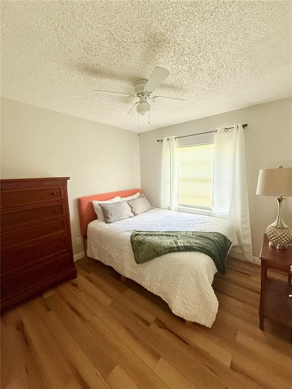 A bedroom features a bed with a coral headboard, a wooden dresser, and wood-look flooring — 9402 N SEMMES STREET, TAMPA, FL