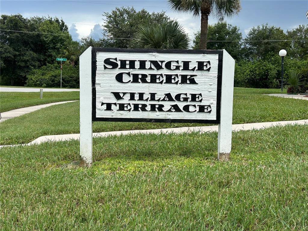 A white sign with black lettering reads Shingle Creek Village Terrace in a grassy area — 3076 SHINGLE CREEK COURT, KISSIMMEE, FL