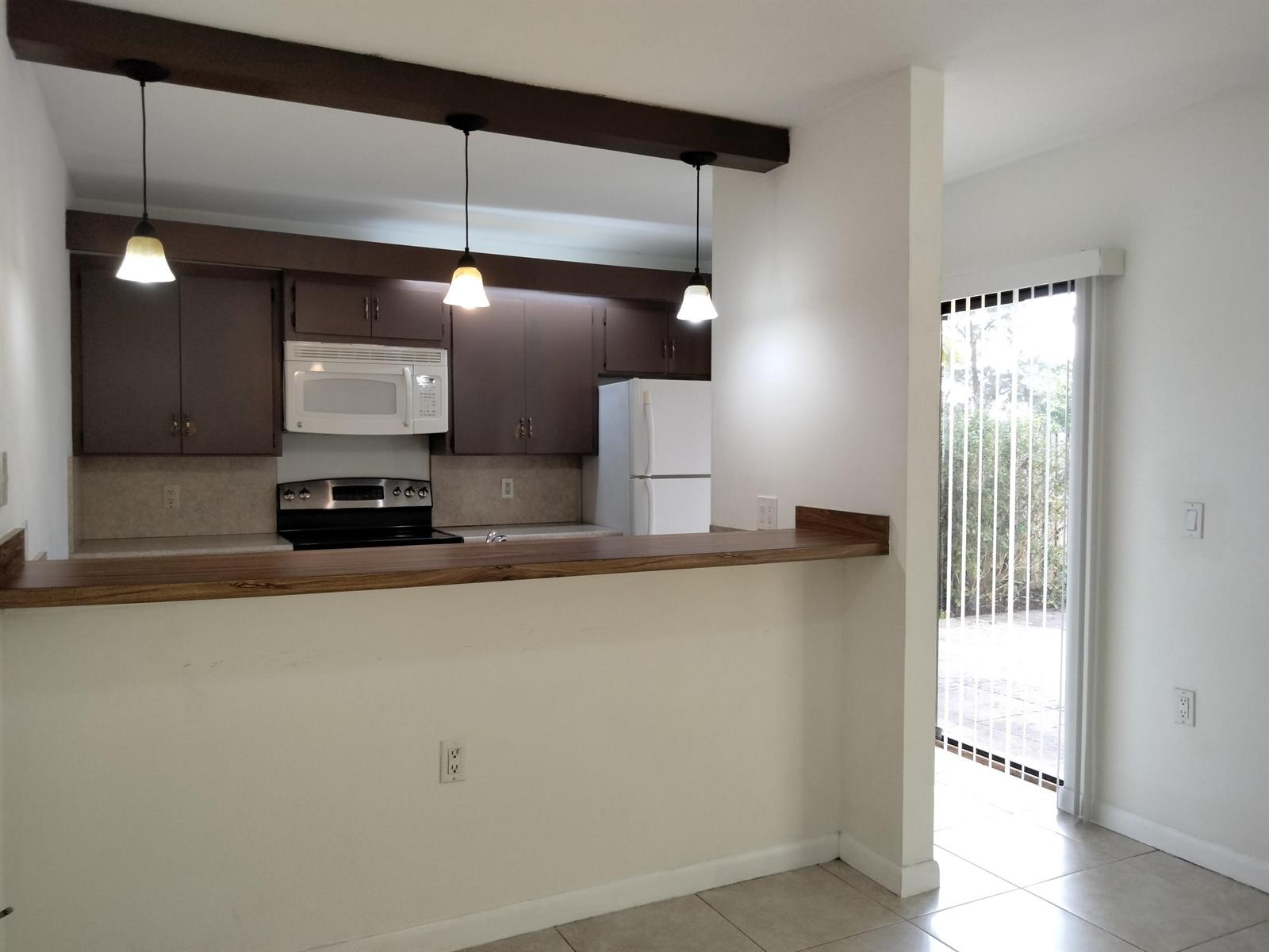 A kitchen with dark wood cabinets and a breakfast bar overlooks a tiled dining area — 4707 47th Way, West Palm Beach FL 33407, WEST PALM BEACH, FL