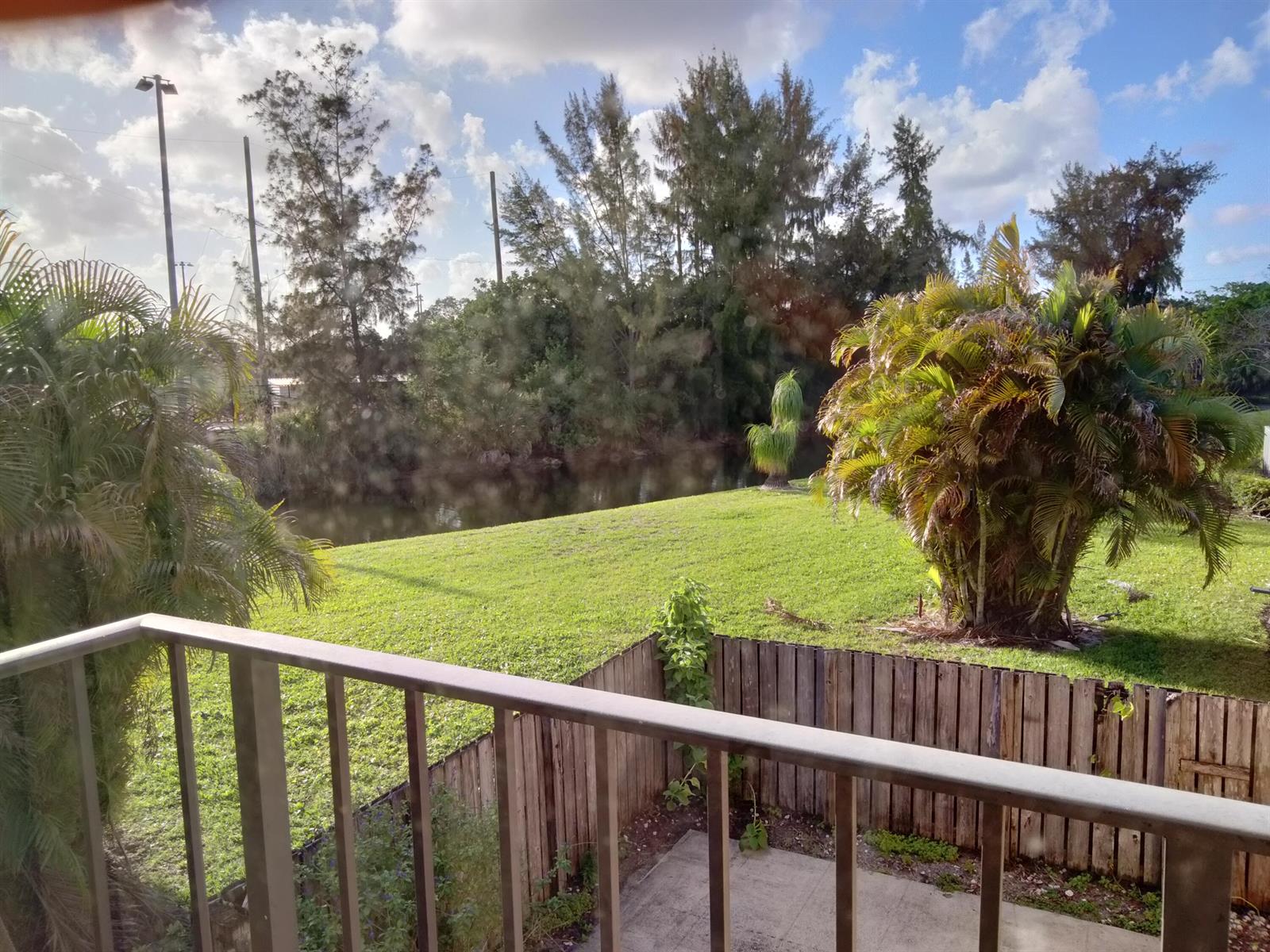 A balcony overlooks a grassy yard, a small canal, and trees under a cloudy sky — 4707 47th Way, West Palm Beach FL 33407, WEST PALM BEACH, FL