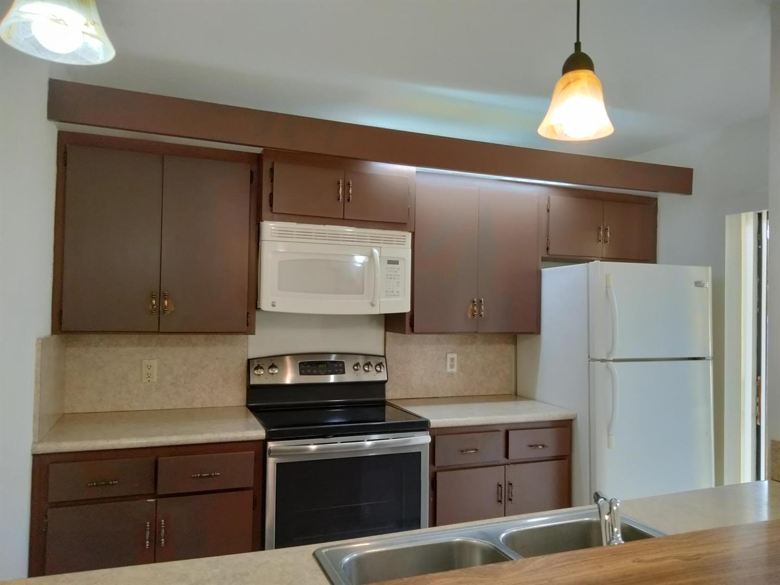 A kitchen features brown cabinets, white appliances, a laminate countertop, and two pendant lights — 4707 47th Way, West Palm Beach FL 33407, WEST PALM BEACH, FL
