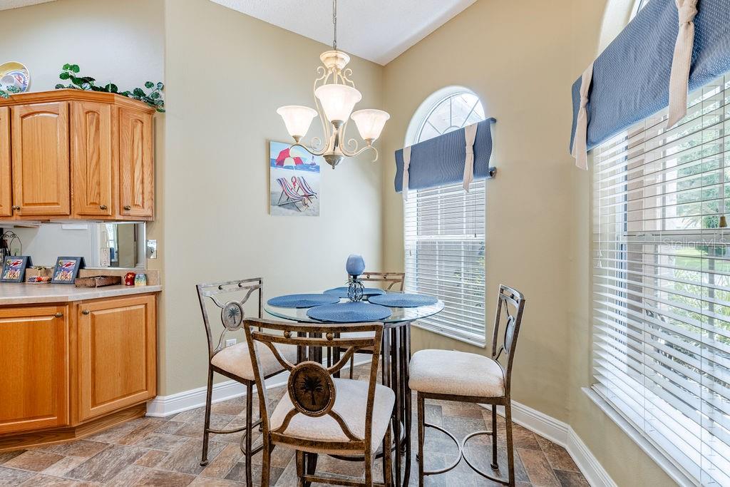 A breakfast nook features a glass-topped table, metal chairs, wood cabinets, and a chandelier — 877 WINIFRED WAY, THE VILLAGES, FL