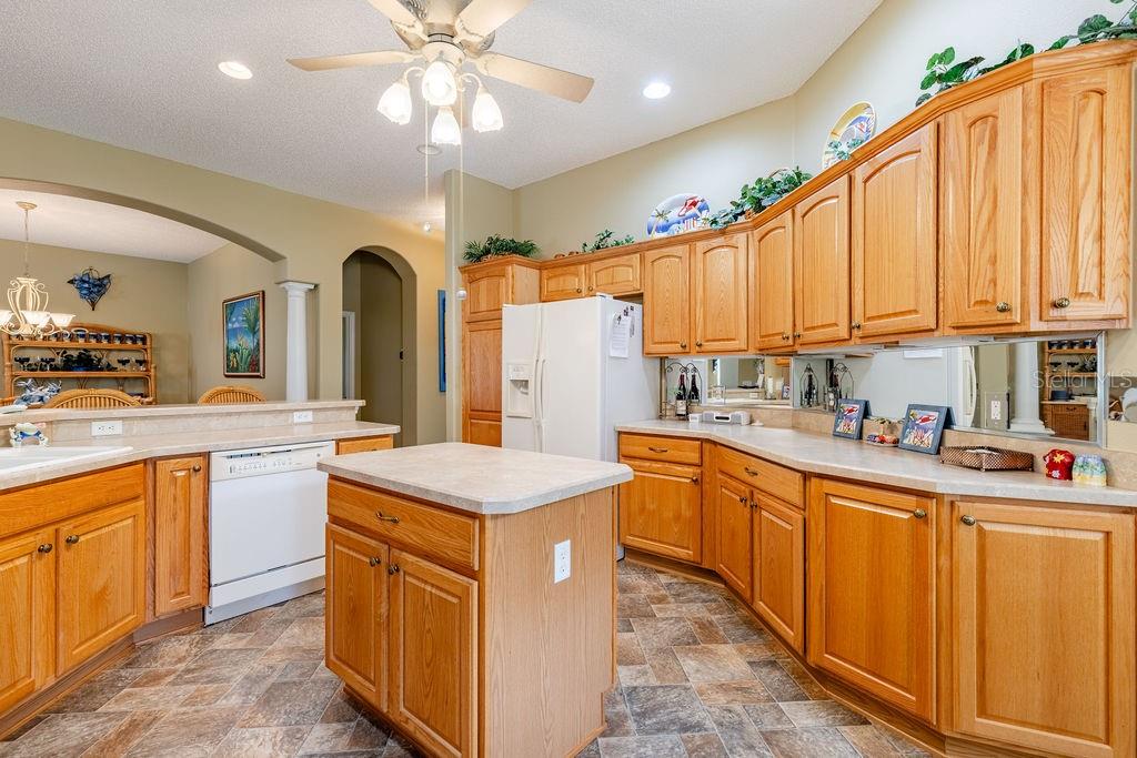 A kitchen features oak cabinets, a central island, white appliances, and a tiled floor — 877 WINIFRED WAY, THE VILLAGES, FL