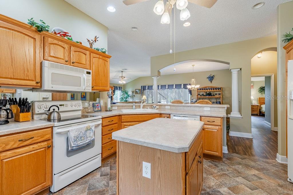 A kitchen features oak cabinets, a central island, white appliances, and tile flooring — 877 WINIFRED WAY, THE VILLAGES, FL