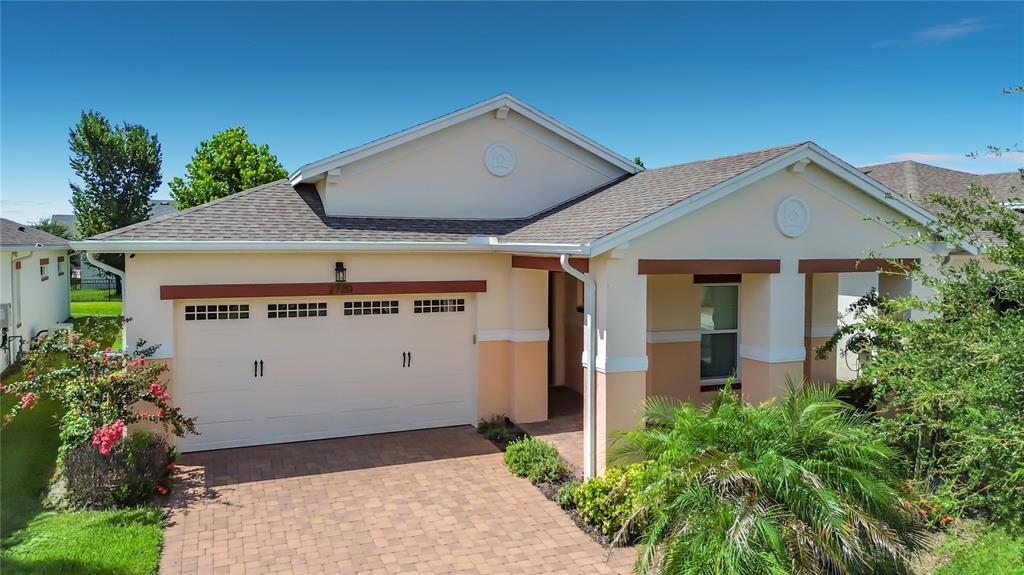 A single-story house with a two-car garage, tan stucco walls, and a paved driveway — 2720 GREENLANDS STREET, ST CLOUD, FL