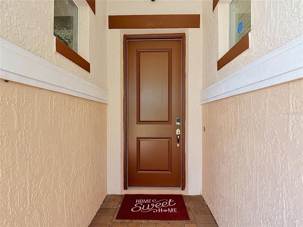 A brown front door is centered between two side windows in a stucco entryway — 2720 GREENLANDS STREET, ST CLOUD, FL
