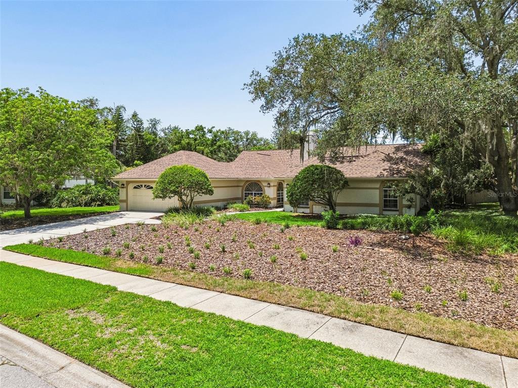 A single-story house with a beige exterior, a brown roof, and a landscaped front yard — 18106 FAIRMEAD COURT, LUTZ, FL