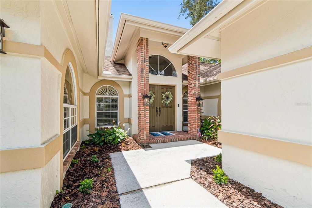 The front entrance of a house features a brick-columned porch and arched windows — 18106 FAIRMEAD COURT, LUTZ, FL