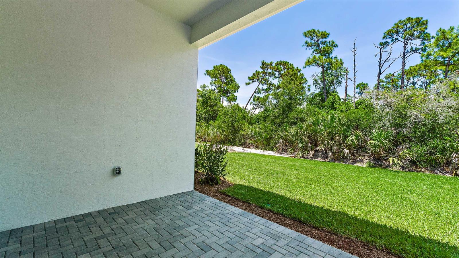 A paved patio overlooks a grassy lawn and a dense line of trees — 212 SE Via Sangro, FL 34952, FL