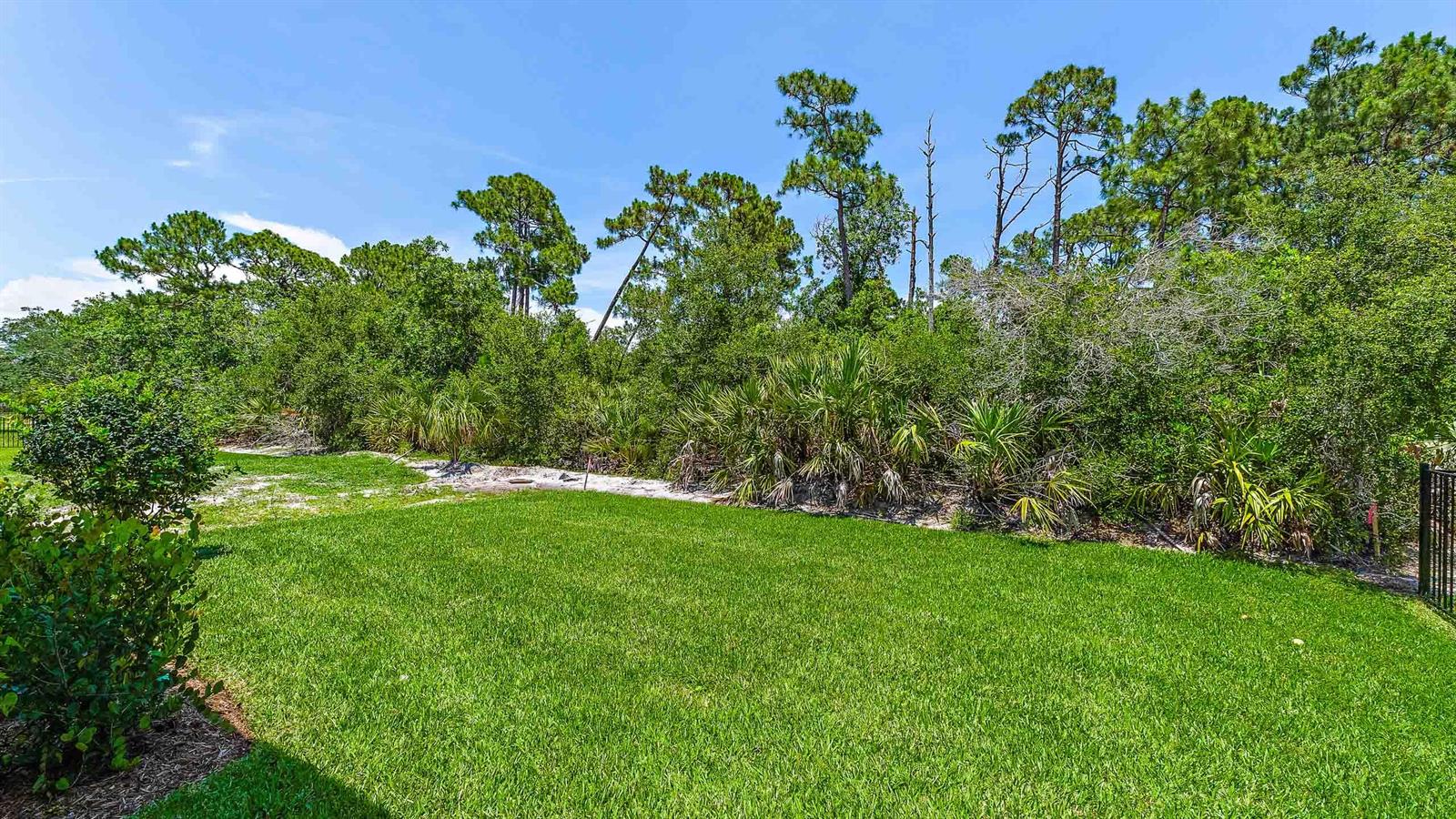 A grassy backyard features a manicured lawn bordered by dense trees and native Florida vegetation — 212 SE Via Sangro, FL 34952, FL