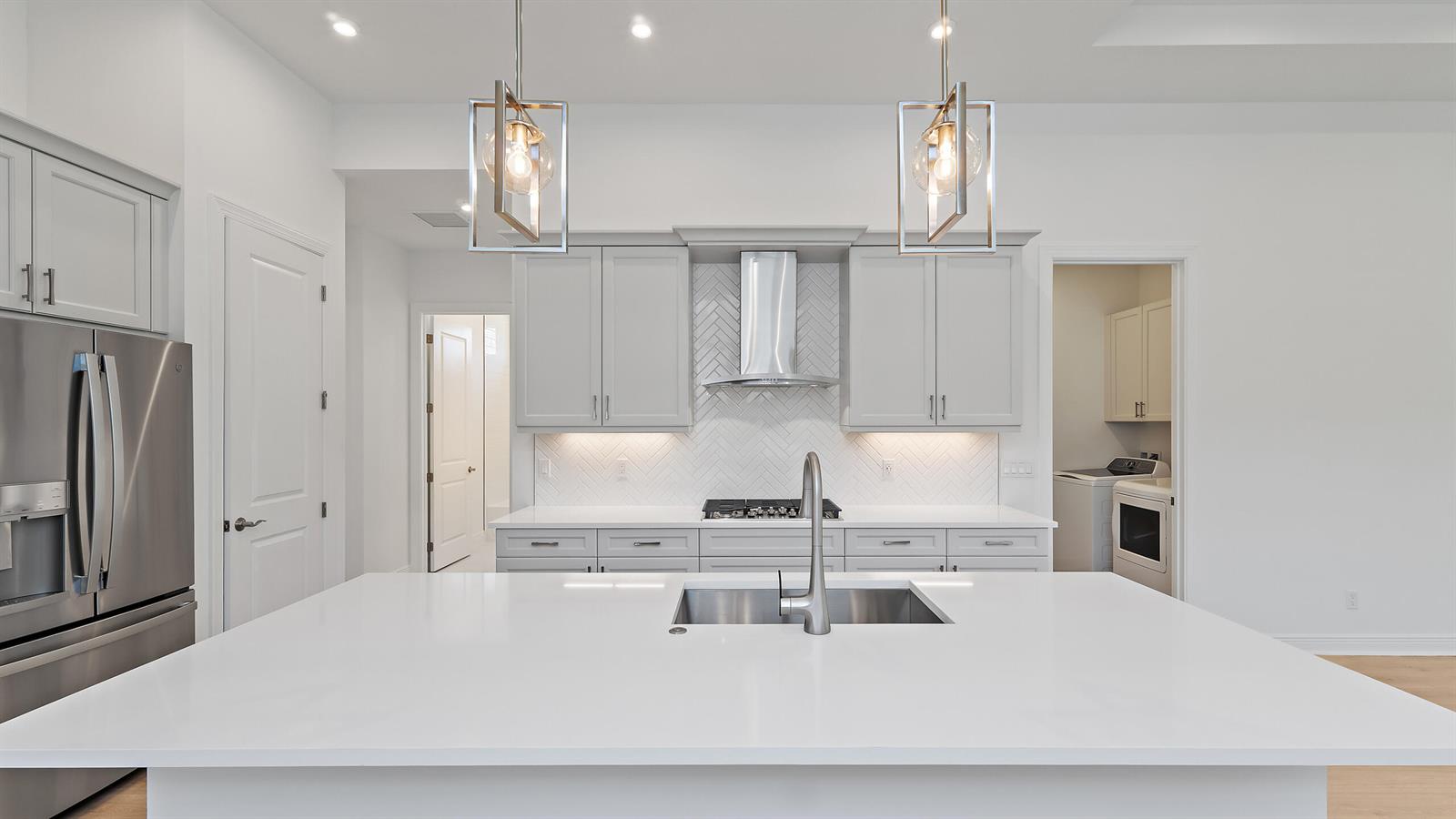 A modern kitchen features light gray cabinets, a white island, and a herringbone tile backsplash — 212 SE Via Sangro, FL 34952, FL