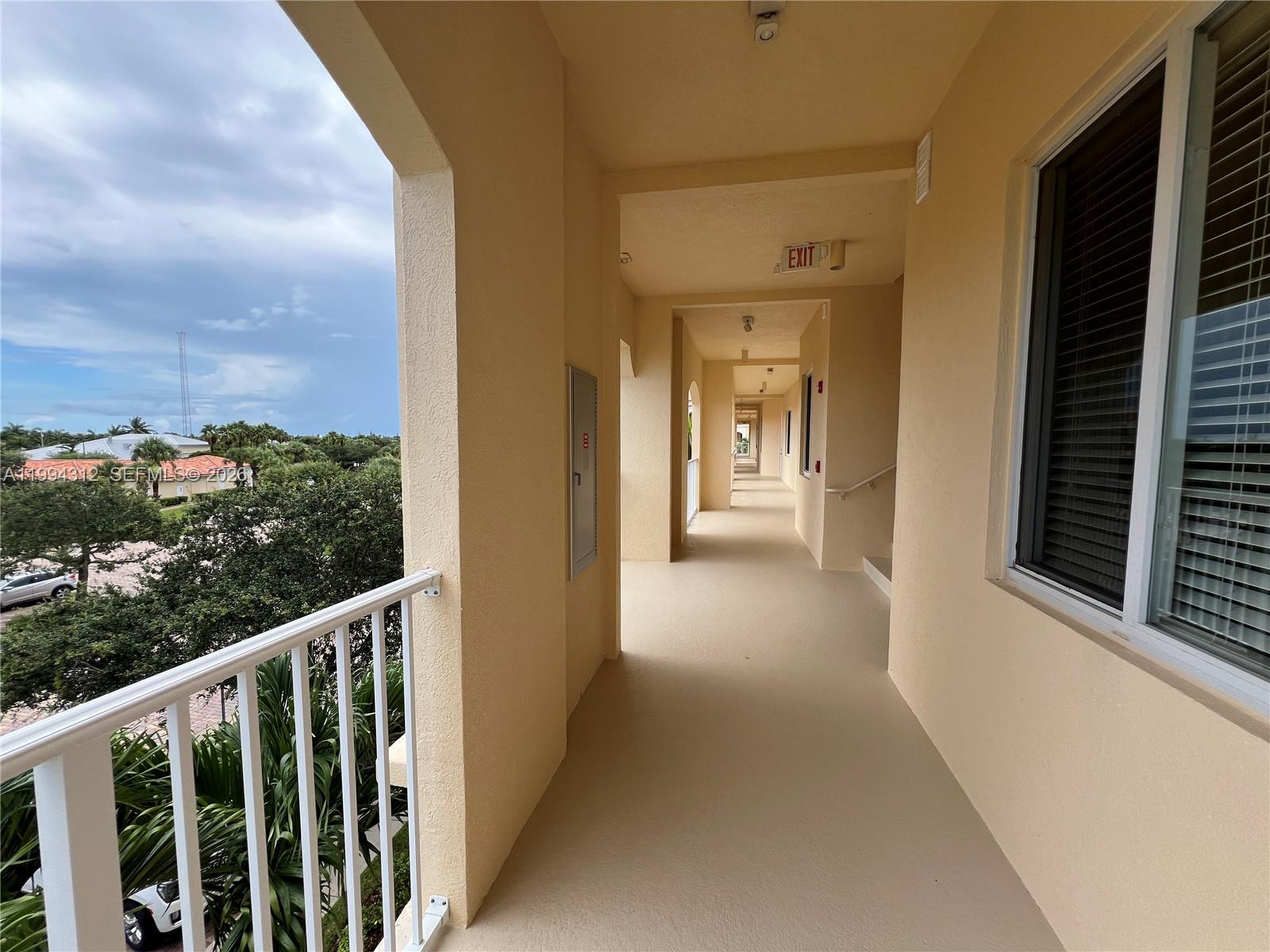 An outdoor covered walkway with beige walls, a white railing, and a view of trees — 5 E Harbour Isle # 306, Fort Pierce FL 34949, FORT PIERCE, FL