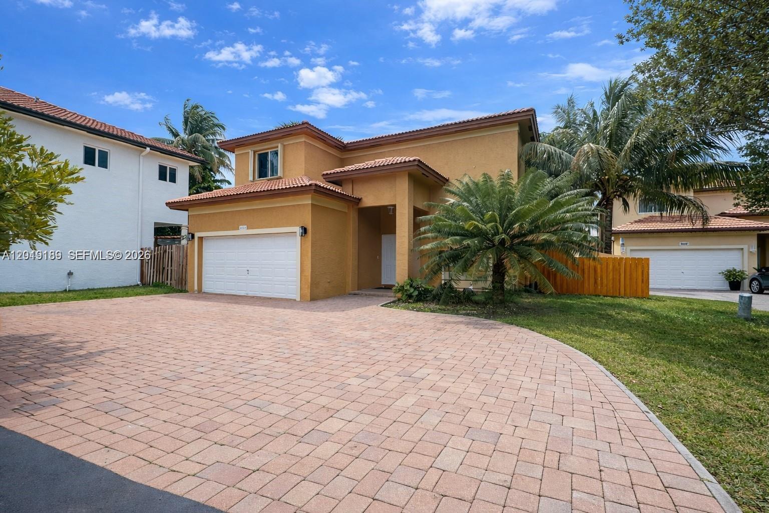 A two-story yellow stucco house features a paved driveway, a two-car garage, and palm trees — 4124 NE 30th St, Homestead FL 33033, HOMESTEAD, FL