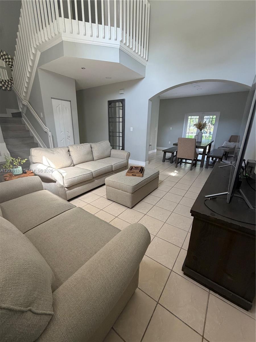 A living room with a staircase, beige sofas, and an arched entryway to a dining area — 4124 NE 30th St, Homestead FL 33033, HOMESTEAD, FL