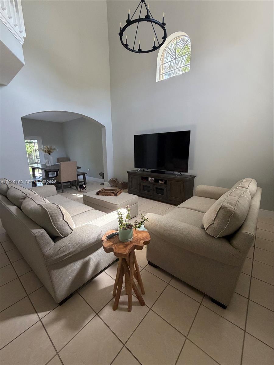 A living room with high ceilings, a chandelier, and two beige sofas facing a television — 4124 NE 30th St, Homestead FL 33033, HOMESTEAD, FL
