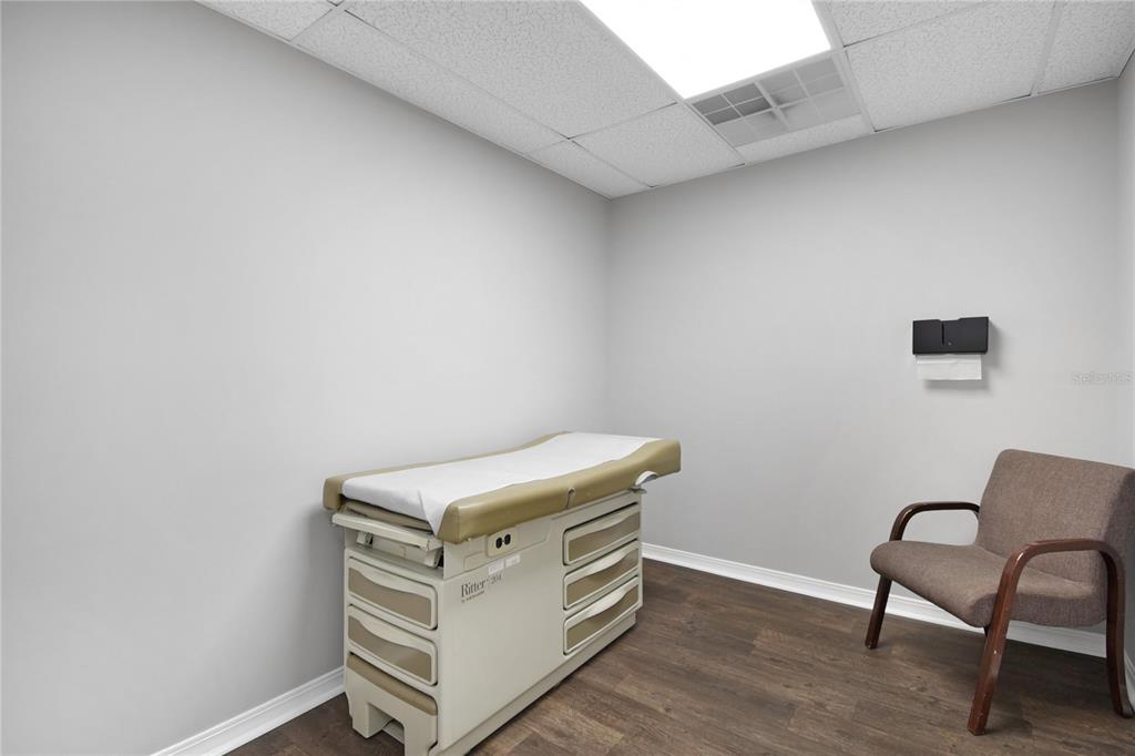 A medical examination room features a beige exam table, a brown chair, and wood flooring — 1840 DUNN AVENUE UNIT 5, JACKSONVILLE, FL