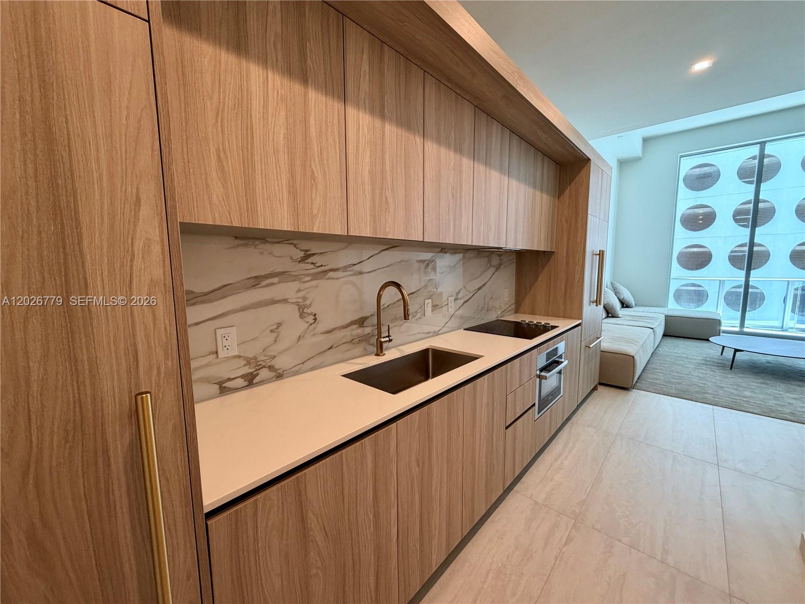 A modern kitchen features wood-grain cabinetry, a marble backsplash, and a stainless steel sink — 77 SE 5th St # 407, Miami FL 33131, MIAMI, FL