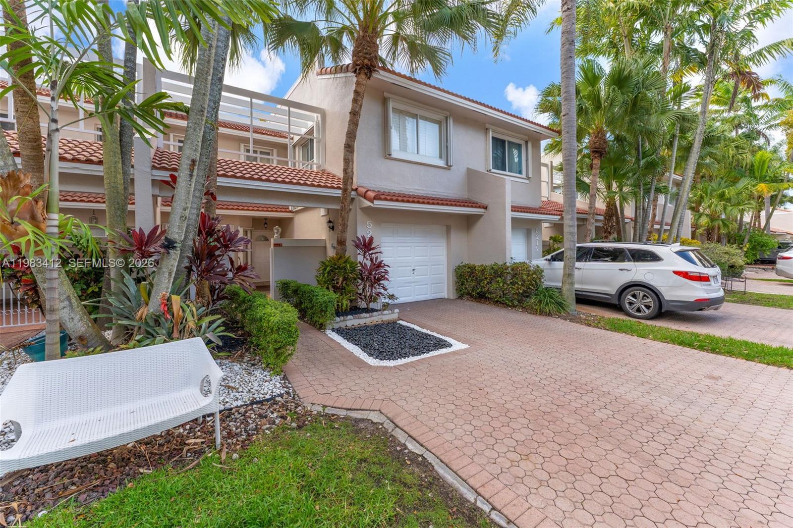 A two-story townhouse features a paved driveway, a white garage door, and palm trees — 5208 NW 103rd Ave, Doral FL 33178, DORAL, FL