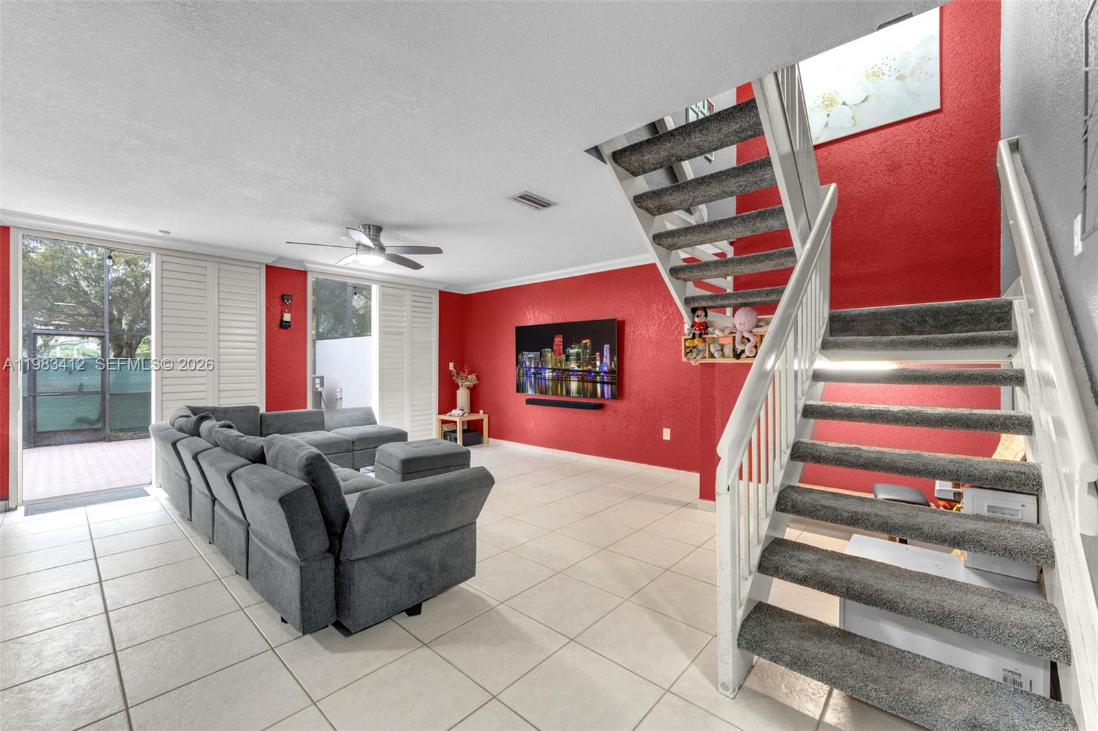A living room features a red accent wall, gray sectional sofa, and carpeted staircase — 5208 NW 103rd Ave, Doral FL 33178, DORAL, FL