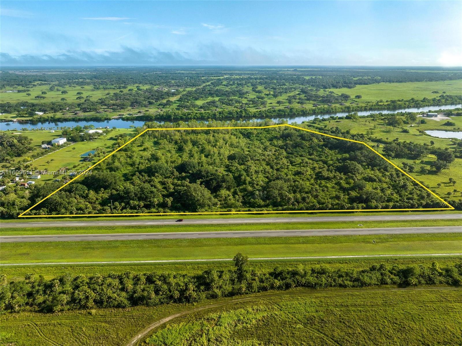 An aerial view shows a rectangular, tree-covered plot of land bordered by a highway and river — 1984 E State Road 80, La Belle FL 33935, LA BELLE, FL