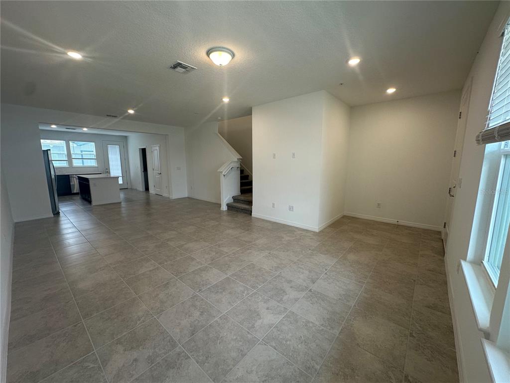 An open-concept living area features light-colored tile flooring, a staircase, and a kitchen beyond — 4620 ORCHARD VIEW ALLEY, CLERMONT, FL