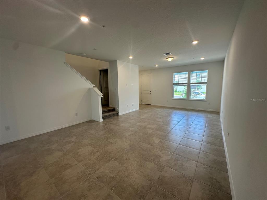 An open-concept living area features light-colored tile flooring, recessed lighting, and a carpeted staircase — 4620 ORCHARD VIEW ALLEY, CLERMONT, FL