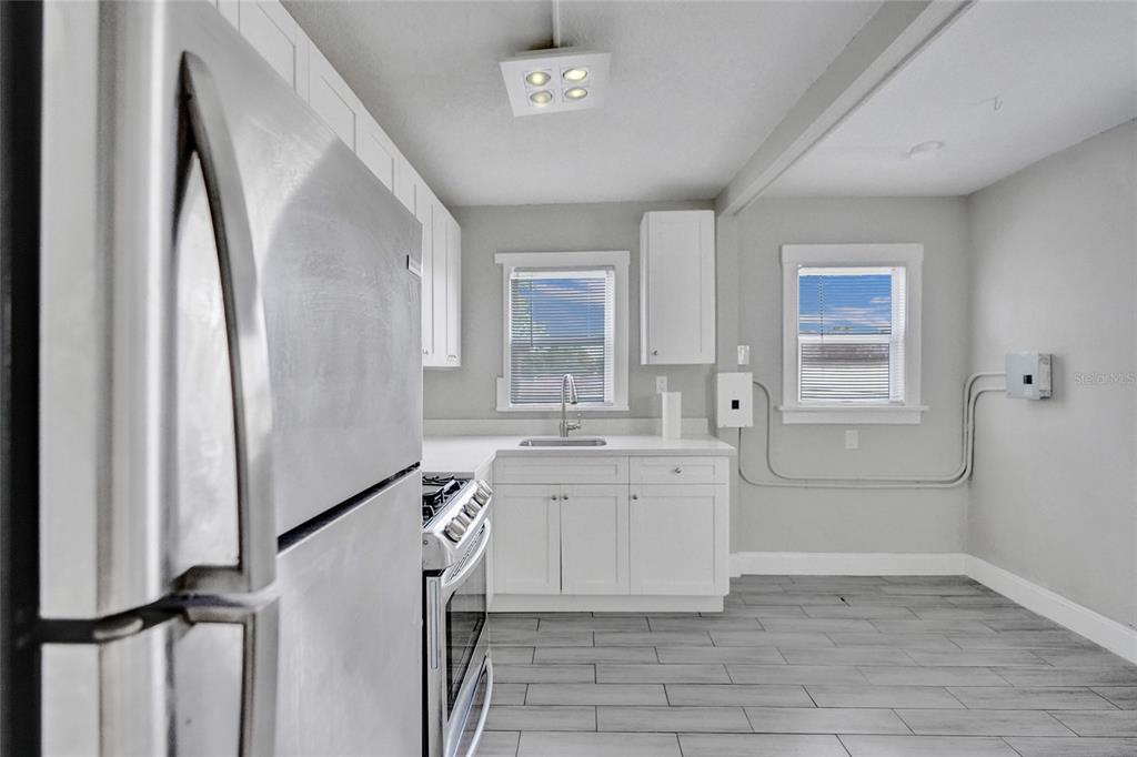 A kitchen features white cabinets, stainless steel appliances, and gray wood-look tile flooring — 924 MCINTOSH STREET, WEST PALM BEACH, FL