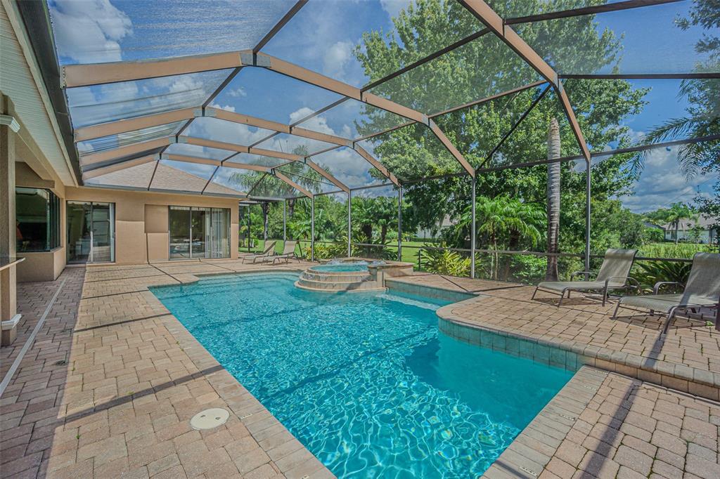 A swimming pool and hot tub sit on a paved patio inside a screened enclosure — 20411 LACE CASCADE ROAD, LAND O LAKES, FL
