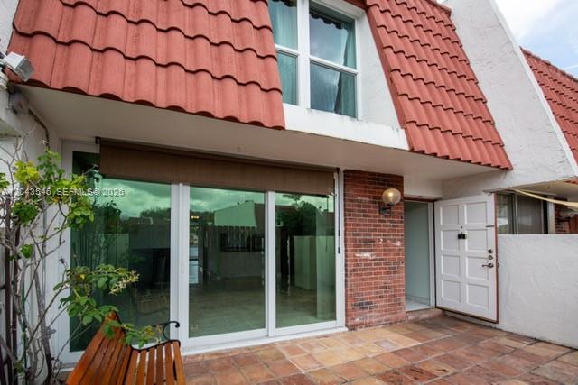 A patio with a wooden bench sits before a sliding glass door and brick wall — 13949 SW 84th St # 801, Miami FL 33183, MIAMI, FL