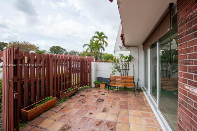 A patio features a wooden bench, terracotta tile flooring, and a brown wooden privacy fence — 13949 SW 84th St # 801, Miami FL 33183, MIAMI, FL