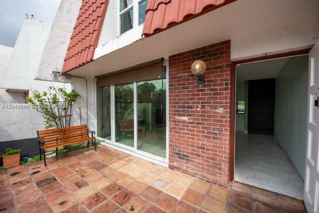 A patio with a wooden bench and brick wall leads into a room through glass doors — 13949 SW 84th St # 801, Miami FL 33183, MIAMI, FL