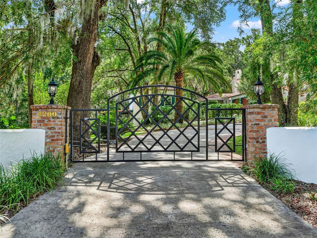 A black metal gate stands between two brick pillars at the entrance of a driveway — 4200 SW 7TH AVE ROAD, OCALA, FL