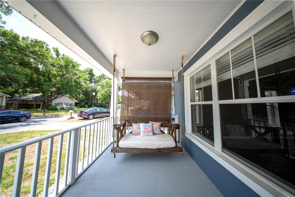 A covered front porch features a hanging wooden swing bed with pillows and white railings — 603 W BELMAR STREET, LAKELAND, FL