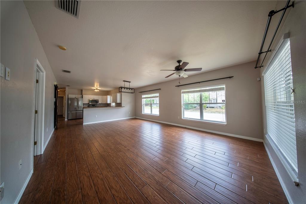 An open-concept living area features wood-look tile flooring, a ceiling fan, and a kitchen beyond — 603 W BELMAR STREET, LAKELAND, FL