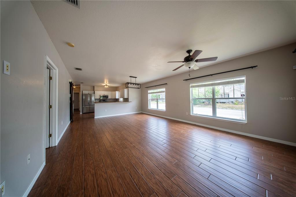 A spacious living room with wood-look tile flooring, a ceiling fan, and an open kitchen — 603 W BELMAR STREET, LAKELAND, FL
