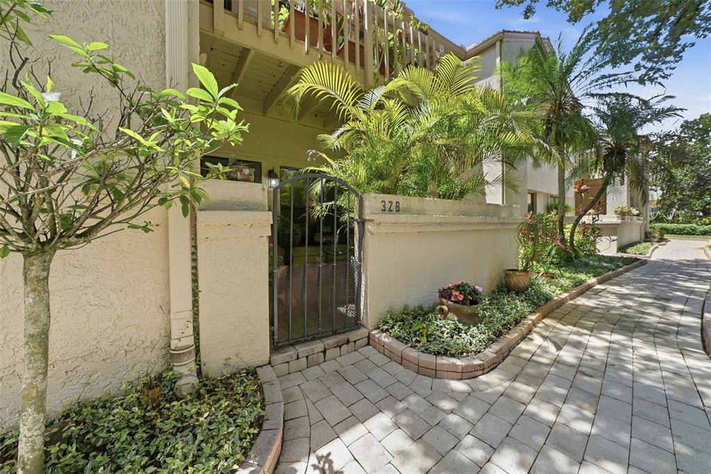 A gated courtyard entrance with a paved walkway and lush landscaping leads to a residence — 328 LOS PRADOS DRIVE UNIT 328, SAFETY HARBOR, FL