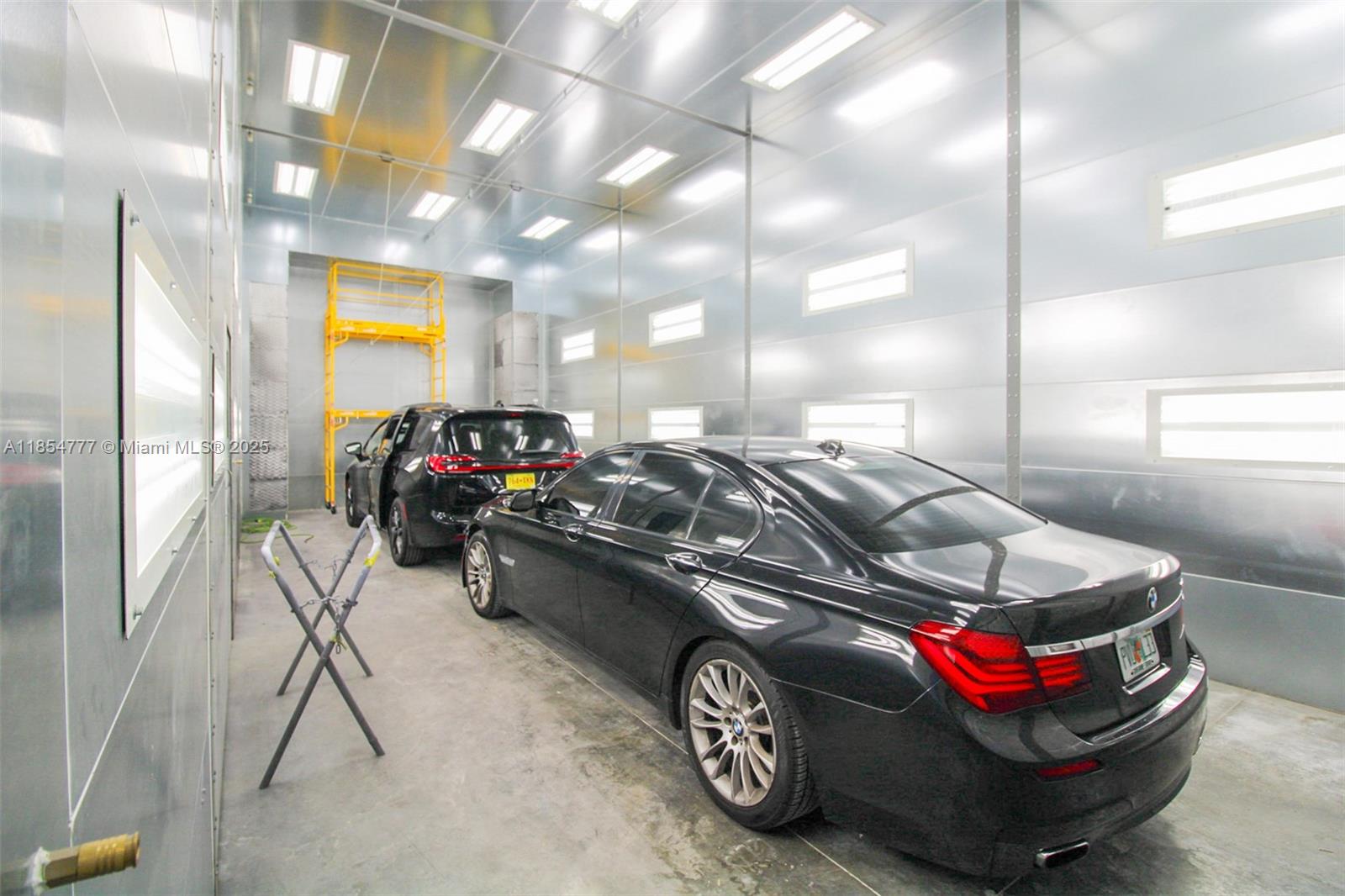 Two black cars are parked inside a metallic, well-lit automotive paint booth — 500 S Dixie Hwy, Hollywood FL 33020, HOLLYWOOD, FL