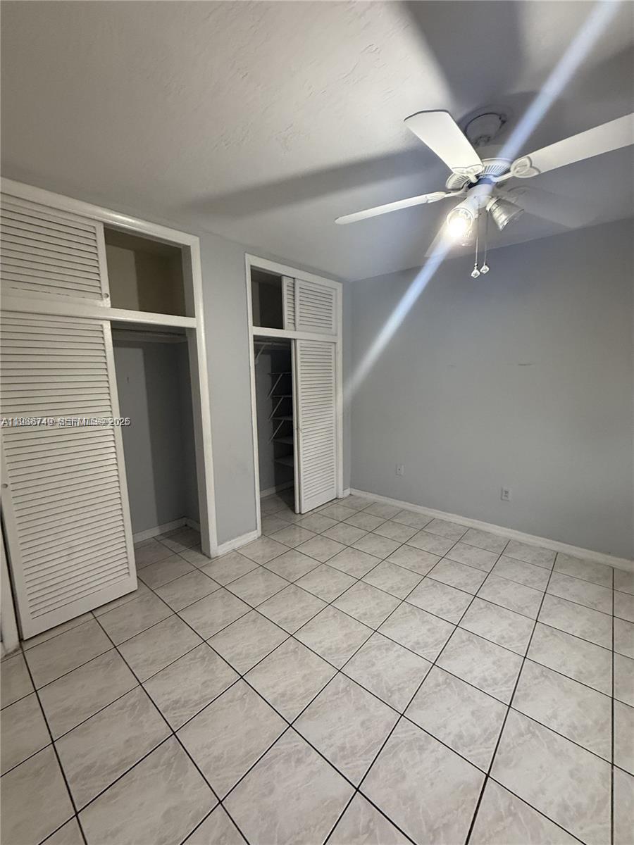 A bedroom with light gray walls, white tile flooring, a ceiling fan, and two closets — 7505 SW 82nd St # 314, Miami FL 33143, MIAMI, FL