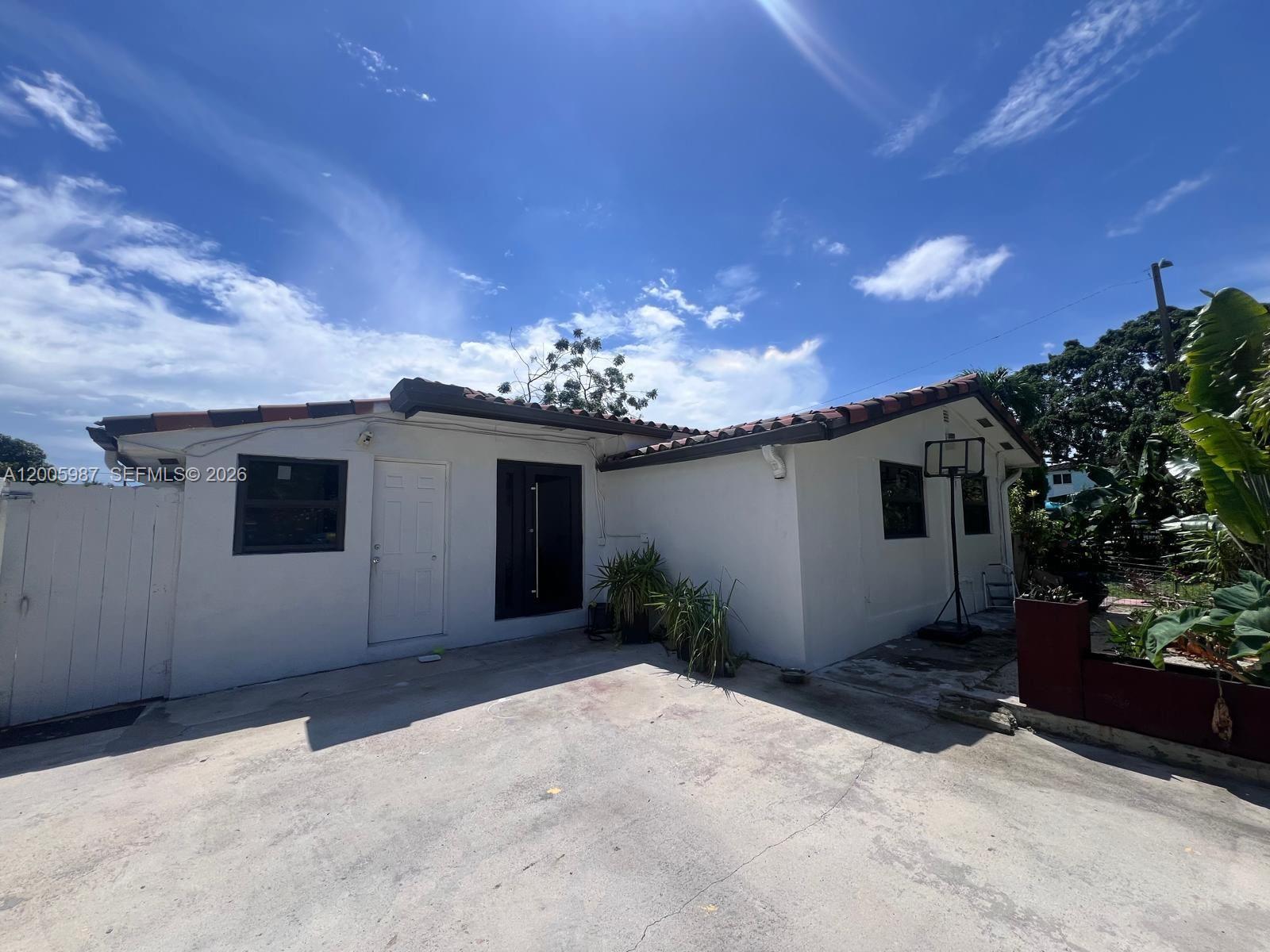 The exterior of a white, single-story house features a concrete driveway and a basketball hoop — 311 NW 32nd Ct, Miami FL 33125, MIAMI, FL