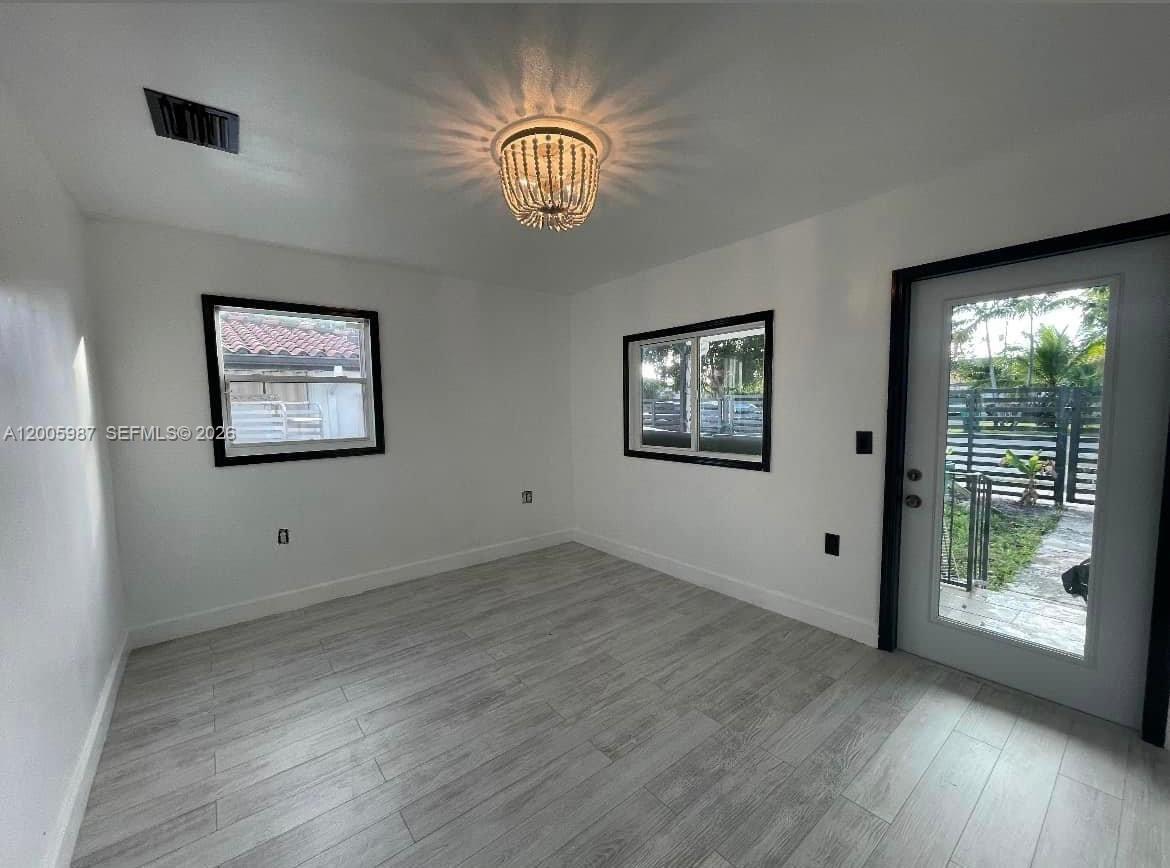 A room with white walls, wood-look tile flooring, a beaded chandelier, and a glass door — 311 NW 32nd Ct, Miami FL 33125, MIAMI, FL
